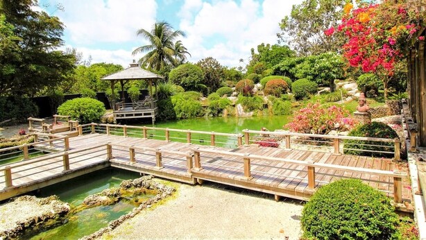 A wooden bridge over a pond with a gazebo and lush greenery. -  Tiny House in Authentic Japanese Koi Garden in Florida (Homestead)
