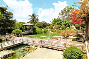 A wooden bridge over a pond with a gazebo and lush greenery. -  Tiny House in Authentic Japanese Koi Garden in Florida (Homestead)