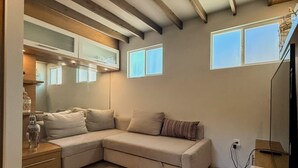 A modern living room with a sectional sofa, wooden flooring, and a sloped ceiling with exposed beams. -  Tiny House in Authentic Japanese Koi Garden in Florida (Homestead)