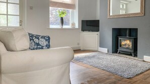 A living room with a sofa, a TV, a fireplace, and a window with a plant. - 3 bedroom accommodation in Buxton (Buxton)