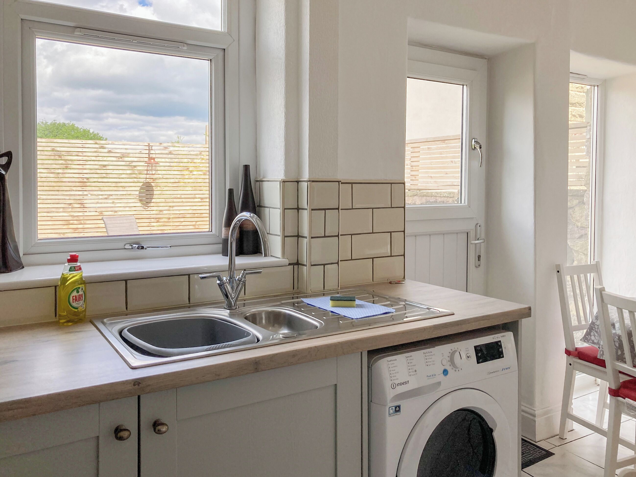 A compact kitchen with a built-in washing machine, a sink, and a window overlooking a garden.