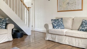 A living room with a beige sofa, a wooden staircase, a map on the wall, and a rug on the floor. - 3 bedroom accommodation in Buxton (Buxton)