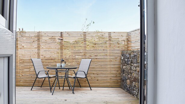 A patio with a round table and two chairs, a wooden fence, and a stone wall. - 3 bedroom accommodation in Buxton (Buxton)