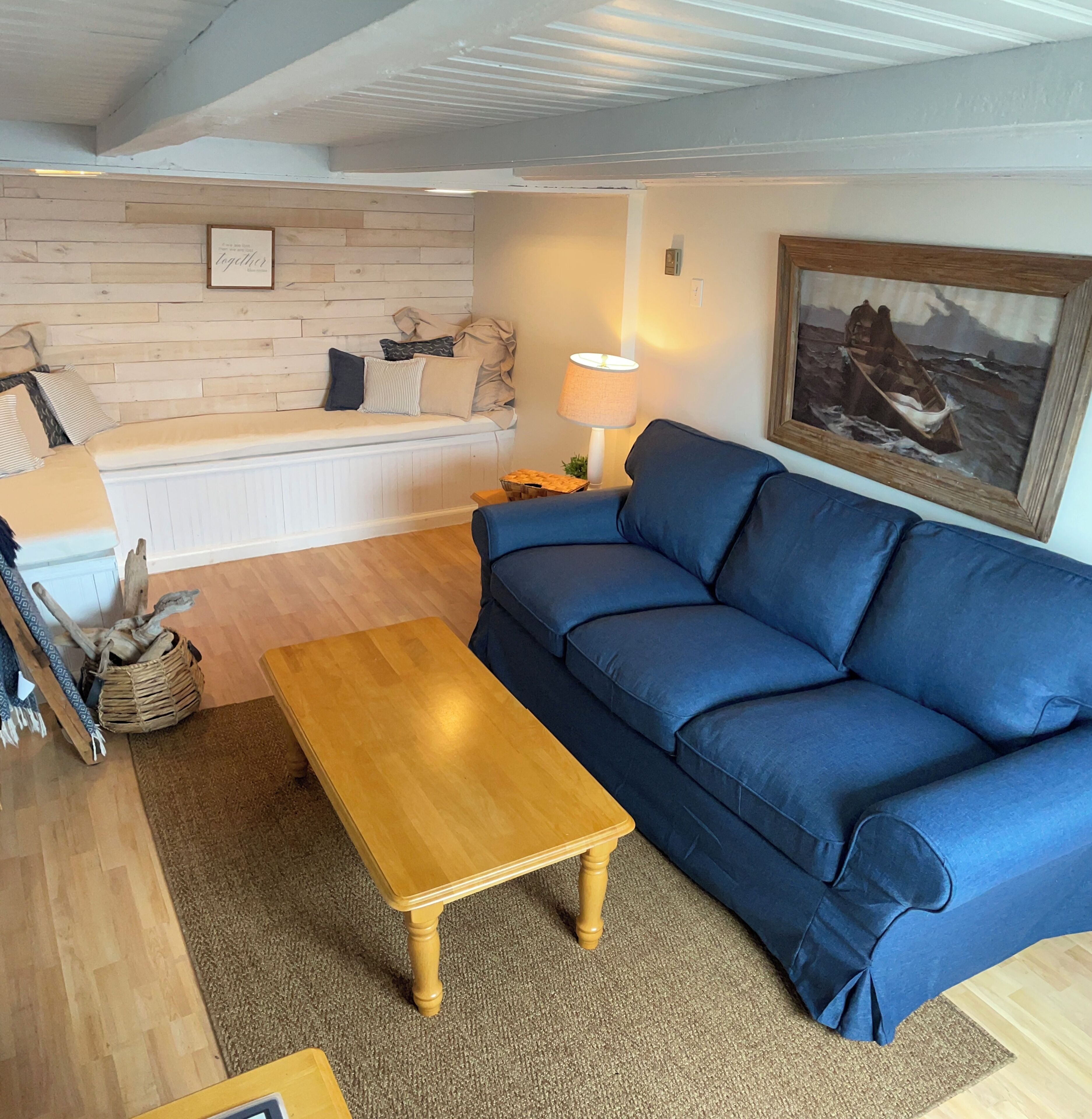 Ein Wohnzimmer mit einem blauen Sofa, einem Holztisch und einem Bild an der Wand.