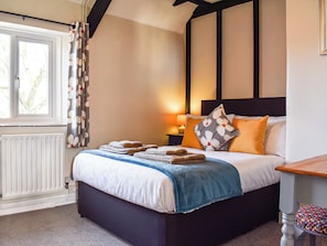 A bedroom with a bed, a nightstand, a lamp, a window with curtains, and a radiator.