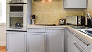 A kitchen with a built-in oven, a toaster, and a range hood. - The Cottage - UK35177 (Buckland Brewer, near Bideford)