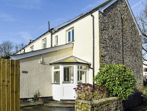 A two-story house with a stone wall, a wooden gate, and a small garden with plants.