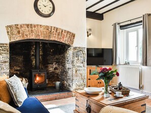 A cozy living room with a brick fireplace, a television, and a dining area with a vase of flowers. - The Cottage - UK35177 (Buckland Brewer, near Bideford)