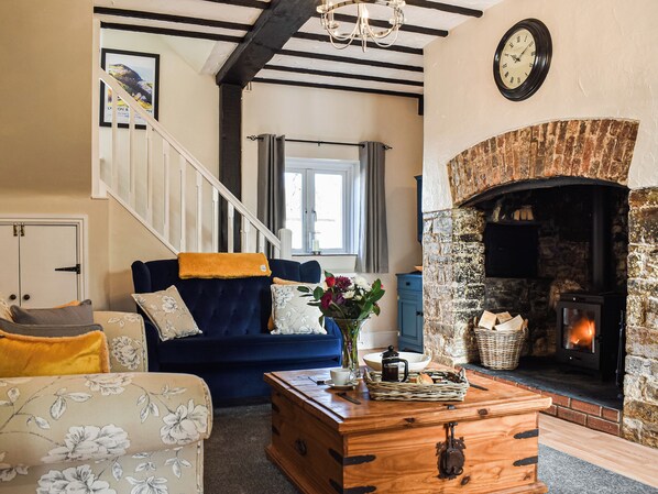 A living room with a fireplace, a staircase, and a blue sofa. - The Cottage - UK35177 (Buckland Brewer, near Bideford)