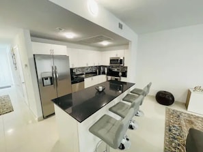 Una cocina moderna con una isla central, electrodomésticos de acero inoxidable y taburetes de bar.