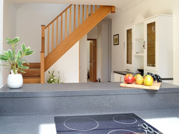 A kitchen with a granite countertop, a wooden staircase, and a dining area with a white cabinet.