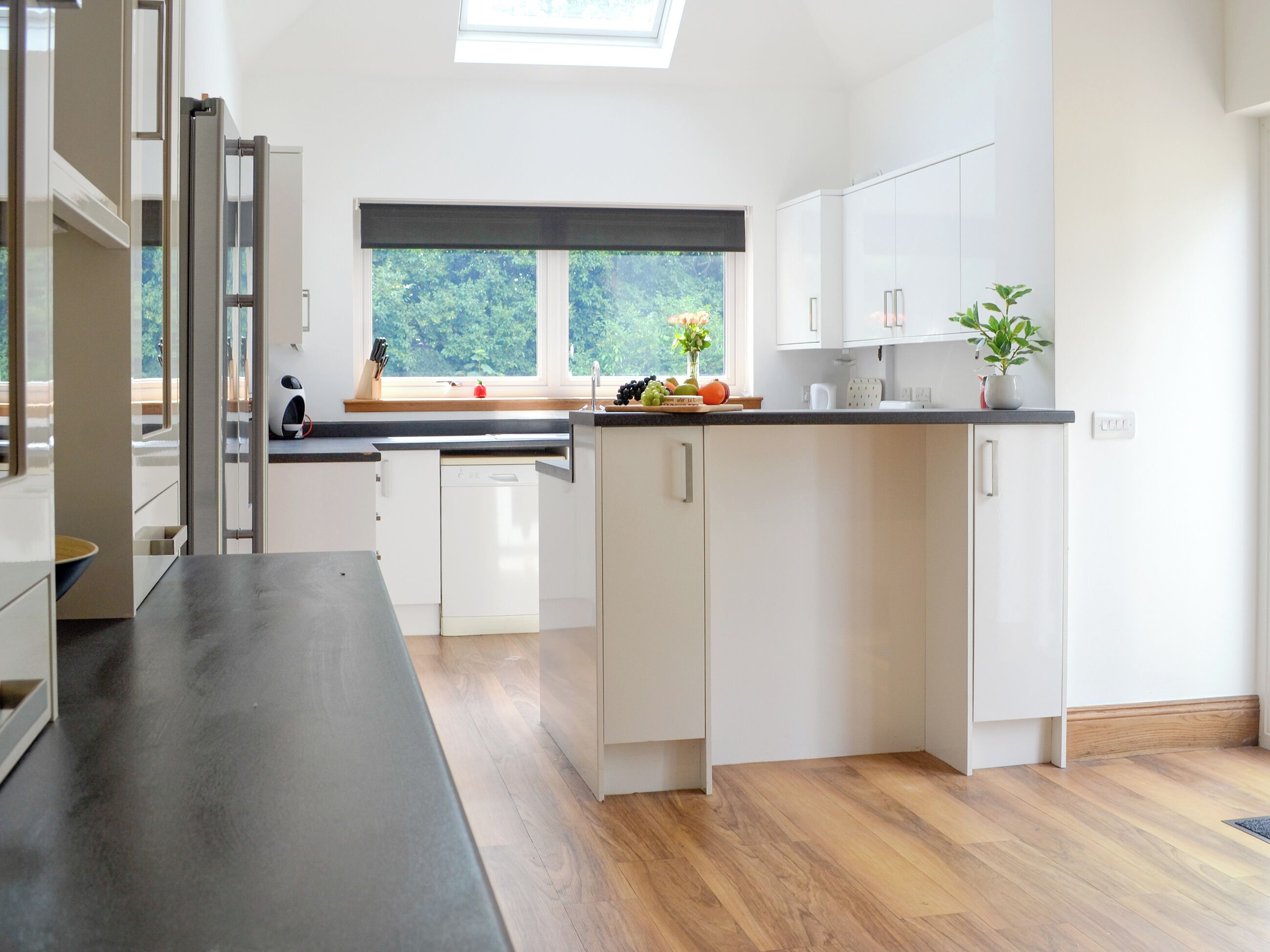 A modern kitchen with white cabinets, a black countertop, and a skylight.