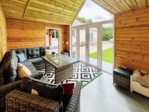 A modern log cabin interior with a sofa, wicker furniture, and a glass door leading outside.