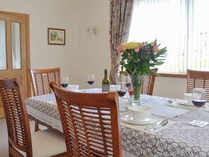 Une salle à manger avec une table dressée pour quatre personnes, agrémentée d’un vase de fleurs, de verres à vin et d’une bouteille de vin.