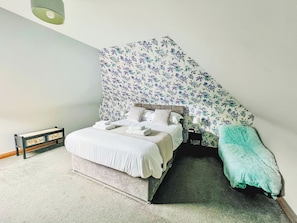 A bedroom with a bed, bedside table, lamp, and a small bench.