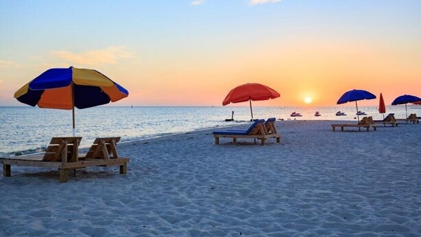 A beach with wooden lounge chairs and colorful umbrellas. - Beachside Gem! Walk to the Beach! Close to Shopping, Dining, & More! (Gulfport)