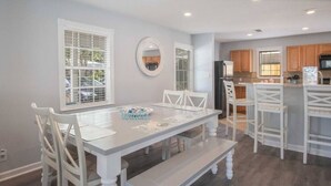 A modern kitchen with white cabinetry, a central island, and a dining area with white chairs and a bench. - Beachside Gem! Walk to the Beach! Close to Shopping, Dining, & More! (Gulfport)