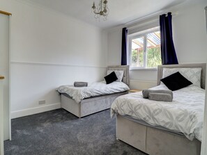 A bedroom with two beds, a window with curtains, a radiator, and a chandelier. - 4 bedroom accommodation in Hayling Island (Hayling Island)