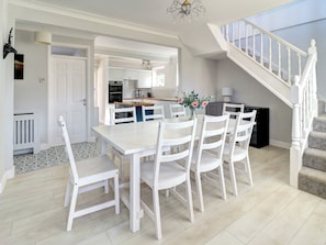A modern kitchen with white cabinetry, a dining area with a white table and chairs, and a staircase with white railings. - 4 bedroom accommodation in Hayling Island (Hayling Island)