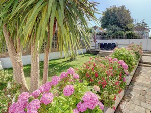 A garden with pink hydrangea bushes, a palm tree, and a white building with a deck. - 4 bedroom accommodation in Hayling Island (Hayling Island)