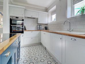 A kitchen with white cabinets, a wooden countertop, a built-in oven, and a patterned floor. - 4 bedroom accommodation in Hayling Island (Hayling Island)