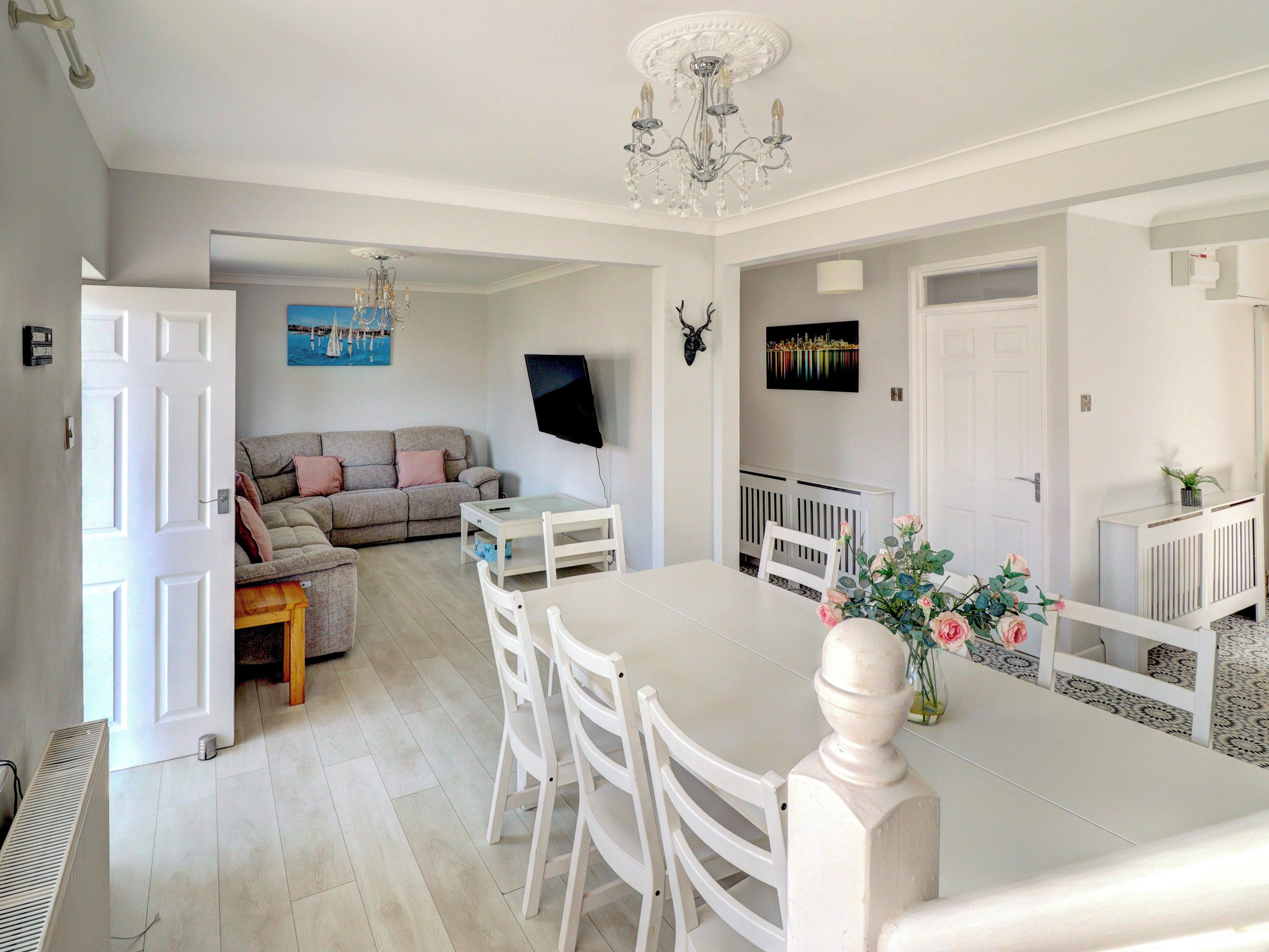 Un salon moderne comprenant un canapé, une table à manger avec des chaises, un téléviseur fixé au mur et un lustre.