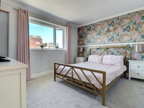A bedroom with a bed, bedside tables, a window with curtains, and a floral wallpaper. - 4 bedroom accommodation in Hayling Island (Hayling Island)