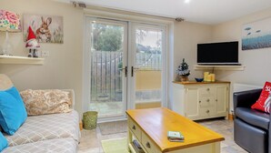 A living room with a sofa, a coffee table, a TV mounted on the wall, and a sliding glass door leading to an outdoor area. - 1 bedroom accommodation in Osmotherley (Osmotherley)