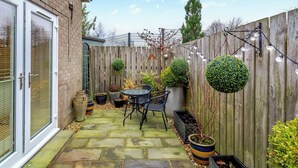 A patio with stone flooring, a table and chairs, potted plants, and a wooden fence. - 1 bedroom accommodation in Osmotherley (Osmotherley)