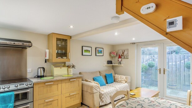 A compact kitchen with a stove, oven, and wooden cabinets. There is a dining area with a table and chairs, and a sofa with cushions. - 1 bedroom accommodation in Osmotherley (Osmotherley)