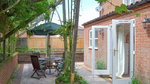 A patio with a round table and chairs, a wooden bench, and potted plants. - Big skies and open beaches galore. (Great Ryburgh)