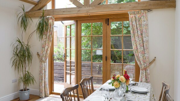 A dining area with a table set for six, wooden chairs, a potted plant, and a view through large windows. - Big skies and open beaches galore. (Great Ryburgh)