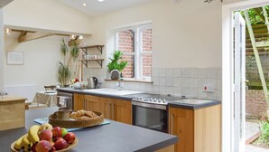 A modern kitchen with a central island, a sink, and a window. There is a bowl of fruit on the island. - Big skies and open beaches galore. (Great Ryburgh)