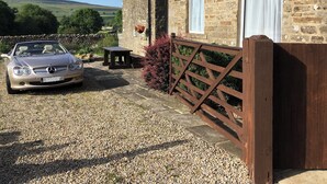 A stone building with a gravel driveway, a parked convertible car, and a wooden gate.
