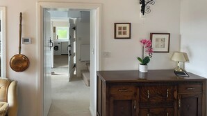 A hallway with a wooden cabinet, a lamp, and a potted orchid. There is a door leading to a laundry area.