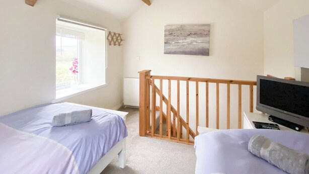 A bedroom with two beds, a window, a painting, a TV, and a wooden staircase.