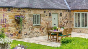 Un bâtiment en pierre avec un toit recouvert de tuiles, une porte verte et une fenêtre aux montants blancs.