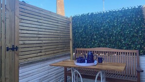 Una mesa de madera con una bandeja de teteras y tazas azules, un banco de madera y una pared de ladrillo.