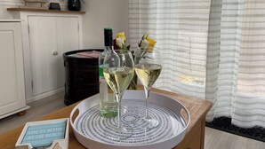 Una habitación con una mesa de madera que sostiene una botella de vino blanco, dos copas de vino y una bandeja con un diseño azul y blanco. Hay una pequeña señal en la mesa que dice 'Life is better at the beach'.