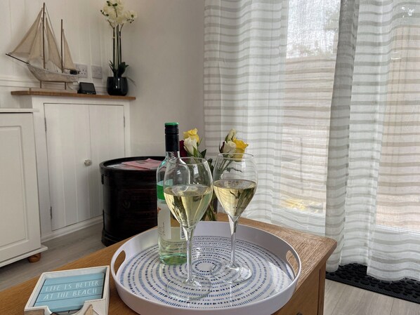 A room with a wooden table holding a bottle of white wine, two wine glasses, and a tray with a blue and white design. There is a small sign on the table that reads "Life is better at the beach."