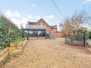 A modern house with a glass extension, a gravel driveway, and a wooden fence. - The Barn at Whitefields (Charlton)