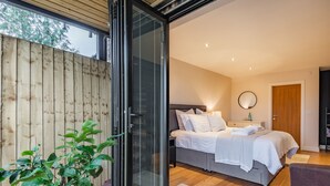 A bedroom with a bed, bedside table, lamp, and a door leading to another room. - The Barn at Whitefields (Charlton)