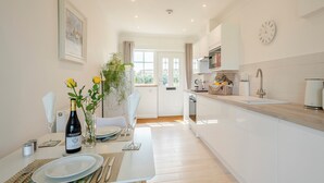 A modern kitchen with white cabinets, a dining area with a table set for two, and a view into the living area. - 1 bedroom accommodation in Ingham, near Stalham (Ingham, near Stalham)