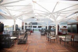 Relax in a spacious outdoor lounge with wicker chairs, tables, and shade from large umbrellas.