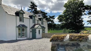 A white building with a green door and windows, a gravel driveway, and a stone sign reading 'DARRIS FARMHOUSE'. - 3 bedroom accommodation in Scaniport (Scaniport)