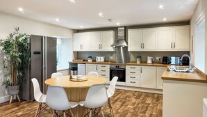 A modern kitchen with white cabinets, a stainless steel range hood, and a dining area with a wooden table and white chairs. - 3 bedroom accommodation in Scaniport (Scaniport)