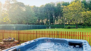 Un bain à remous dans un jardin, avec une clôture en bois, un bac à fleurs en briques et un étang en arrière-plan.