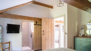 Une chambre à coucher comprenant un lit, une chaise en bois, un téléviseur, une commode et une porte donnant sur une autre pièce.