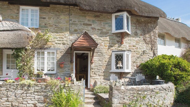 A stone cottage with a thatched roof, a wooden door, and a small porch with steps leading to the entrance. - 1 bedroom accommodation in Batson (Batson)