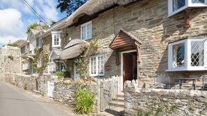 A stone cottage with a thatched roof, a wooden door, and a small porch with a bench. - 1 bedroom accommodation in Batson (Batson)